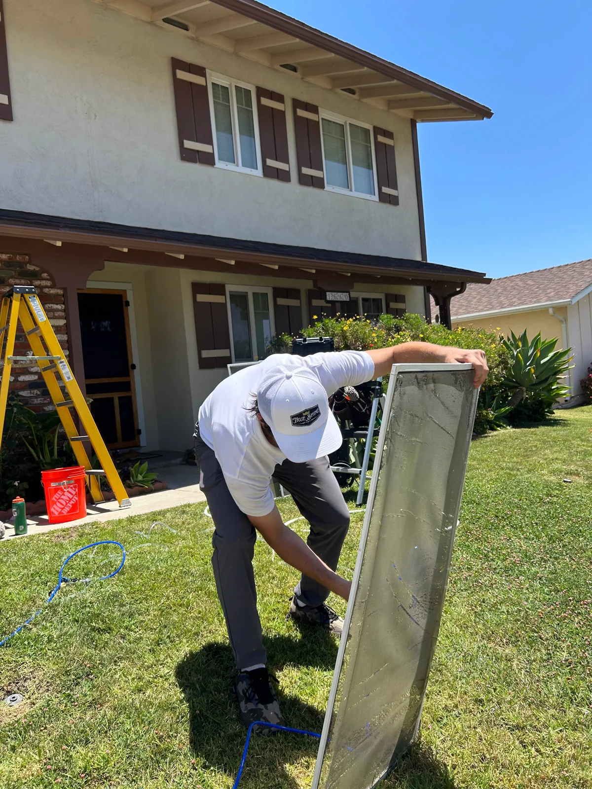 A True Shine technician cleaning a window screen outside a home