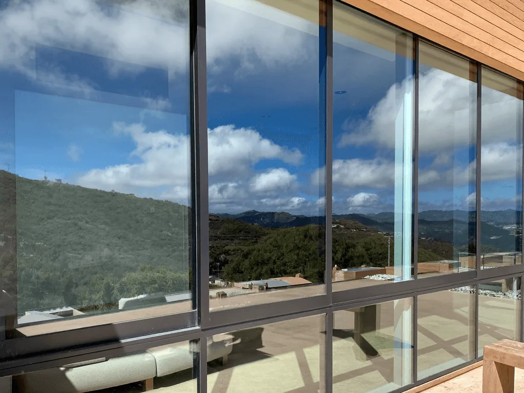 Crystal-clear hillside-view windows reflecting blue sky and clouds