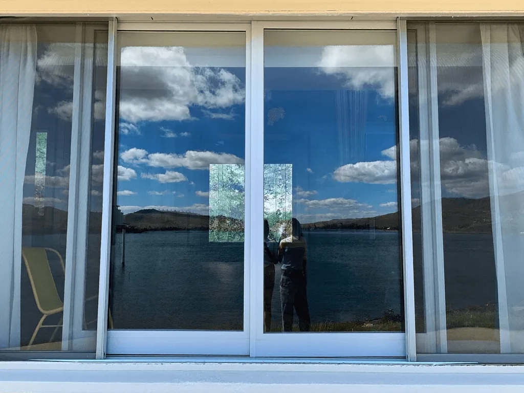 Technician cleaning a large lakefront sliding glass door reflecting blue sky