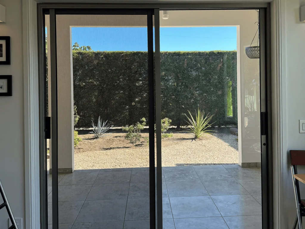 Clean sliding glass doors framing a desert-landscaped patio and hedge