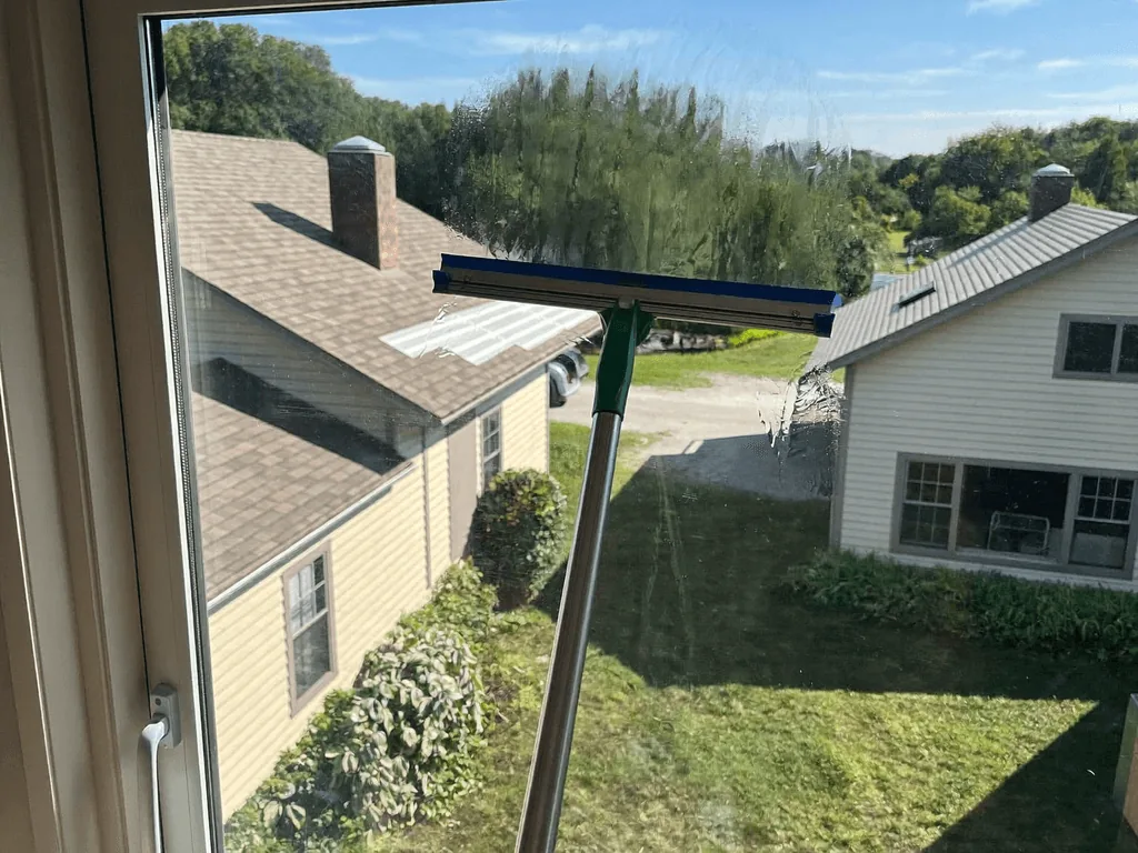 Technician squeegeeing water off a window overlooking sunny neighboring homes