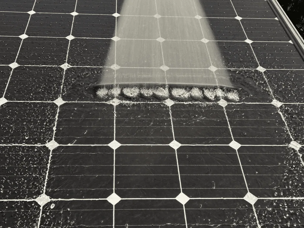 Water rinsing across a grimy black solar panel during professional cleaning