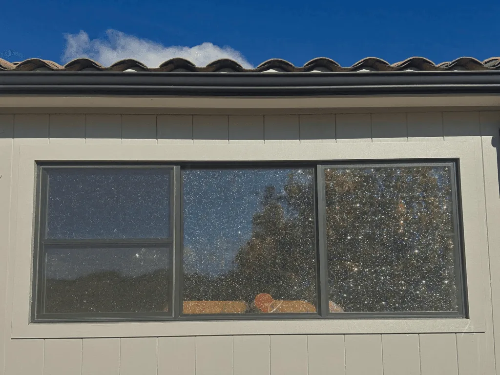 Dirty exterior windows covered in hard water spots beneath a tile roofline