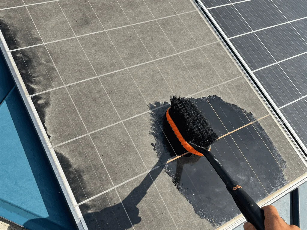 Technician scrubbing a dusty solar panel with a cleaning brush