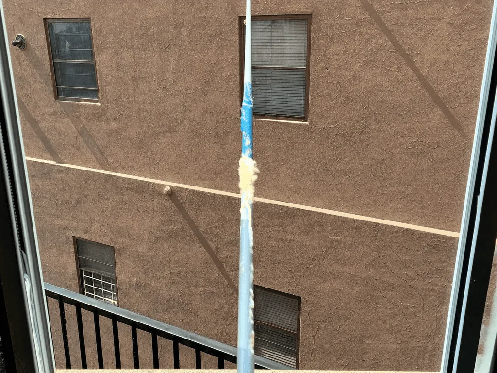 Water-fed pole cleaning an apartment window above a balcony